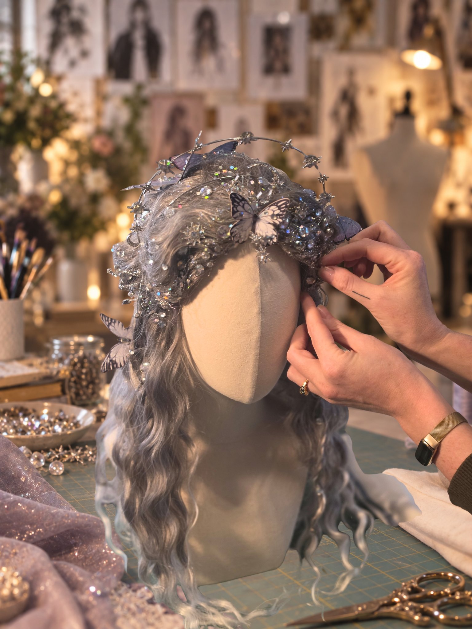 Hands arranging a silver butterfly and star headpiece on a mannequin in a warmly lit costume studio